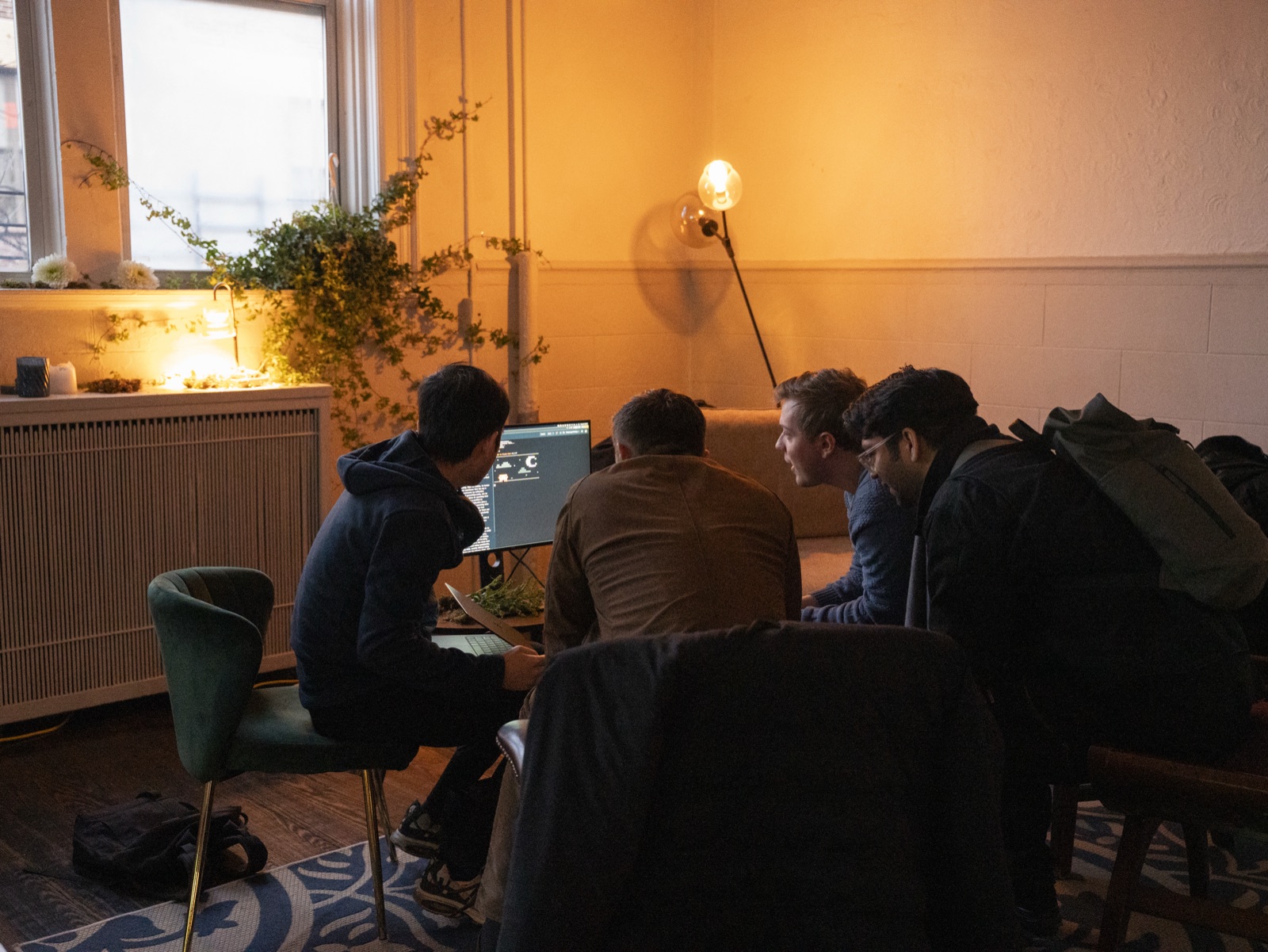 A local AI demo at the Brooklyn meetup — three people gathered around a laptop in a side study, a houseplant on the radiator, warm lamp light. The Grove, Greenpoint.